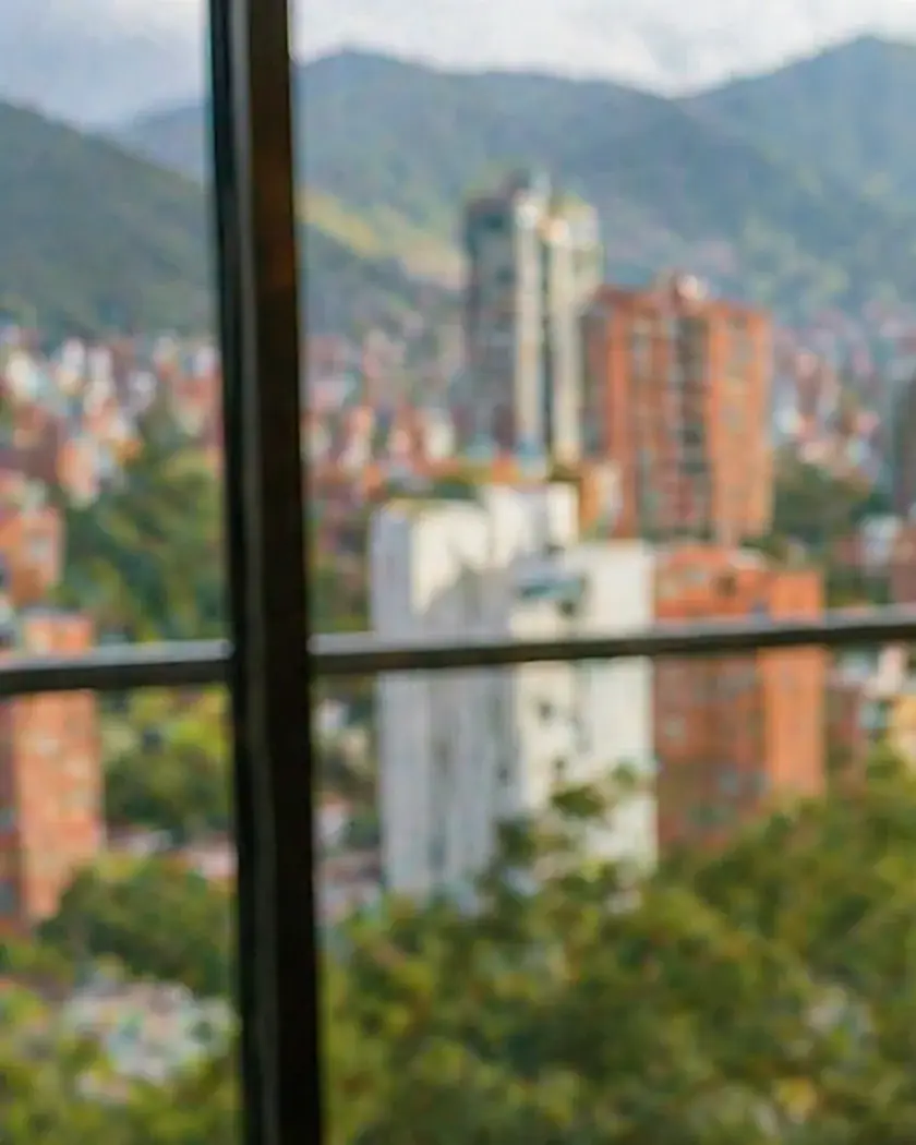 Vista de edificios y montañas de Medellín a través de un ventanal con marco oscuro, desde un apartamento en Belén