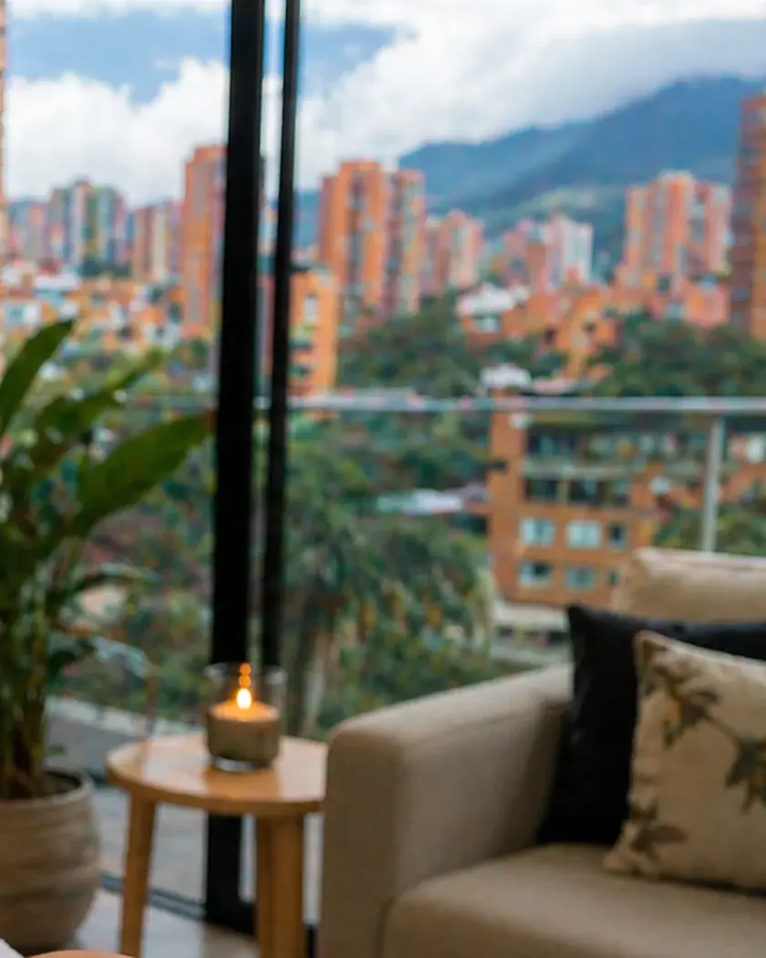Sala con vela encendida y ventanal con vista a los edificios y montañas del sur del Valle de Aburrá, en Itagüí